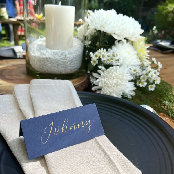Navy place card with gold ink on wedding table with white flowers and candle